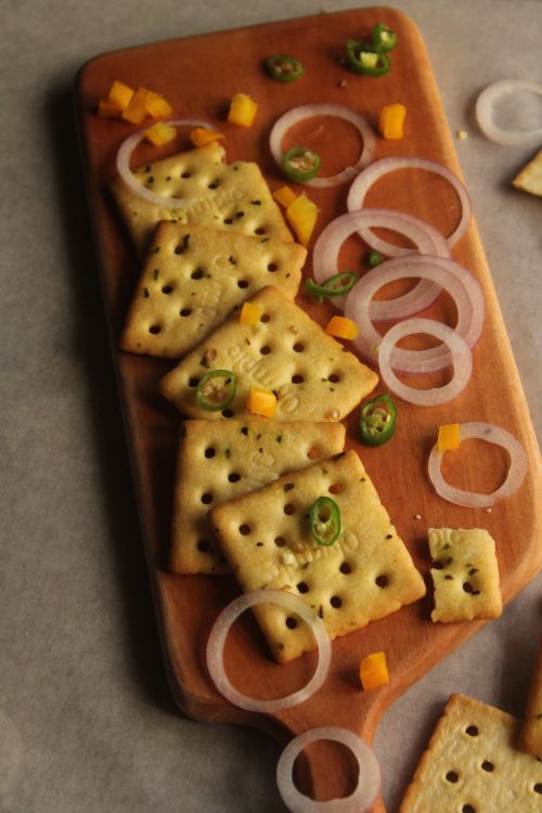 Free Flat lay of cheesy crackers garnished with onion rings and chopped peppers. Stock Photo