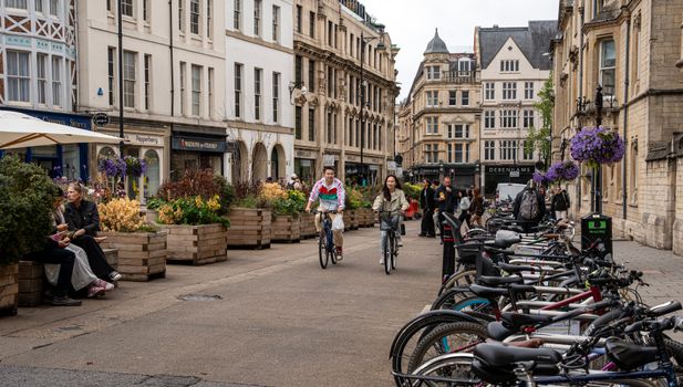 People bicycling and enjoying a lively street in Oxford with historic architecture.