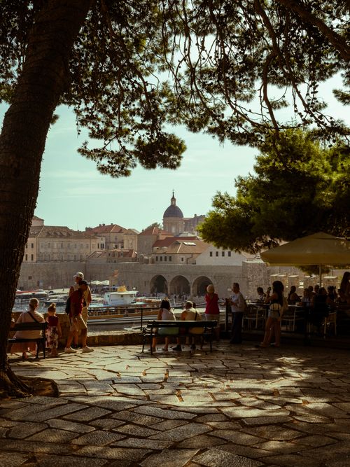 Free Charming view of Dubrovnik's harbor and city walls with people enjoying leisure time in a waterfront café. Stock Photo
