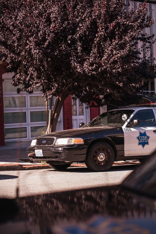 Free Police vehicle parked in a sunlit San Francisco neighborhood, surrounded by urban architecture. Stock Photo