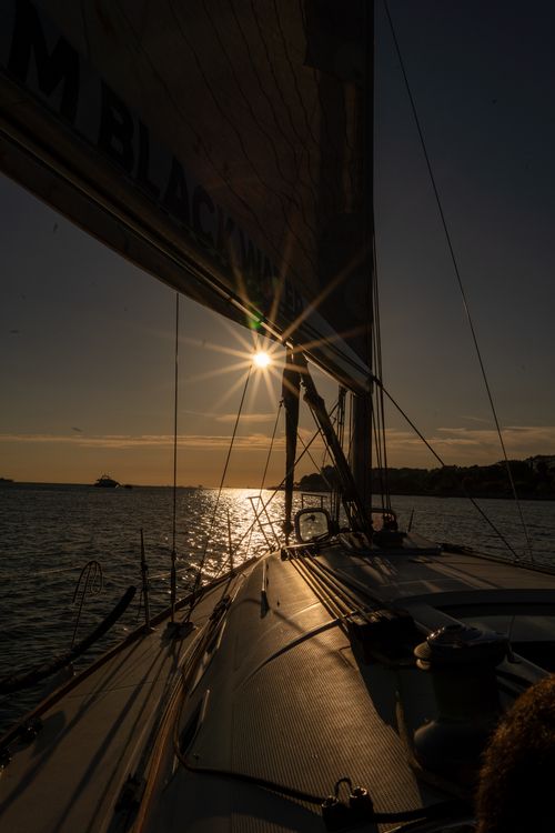 Free Serene view from a sailboat deck at sunset, capturing the sun's flare over calm waters. Stock Photo