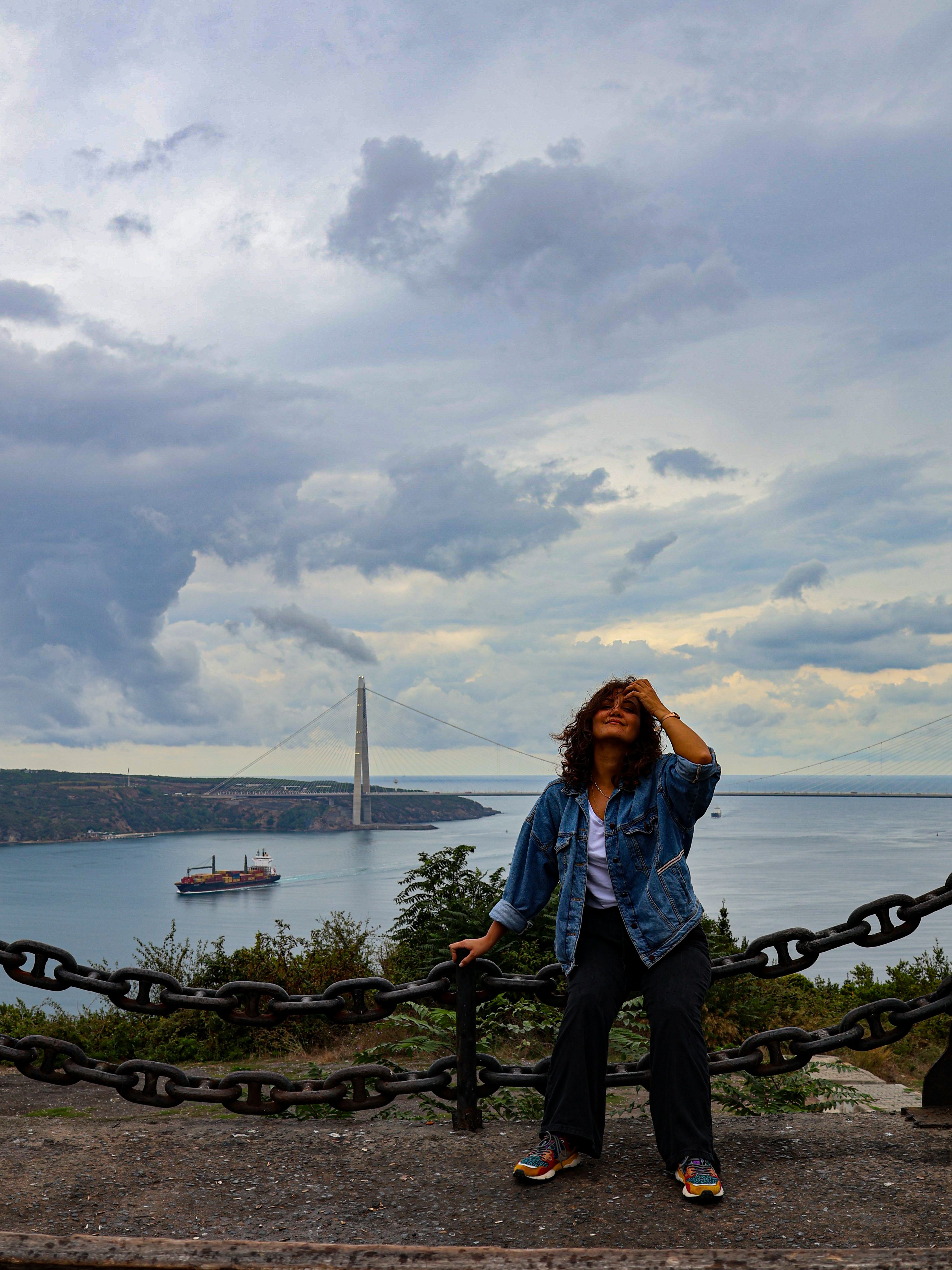 A woman sits by Bosphorus with Yavuz Sultan Selim Bridge in the background, Istanbul, Turkey.
