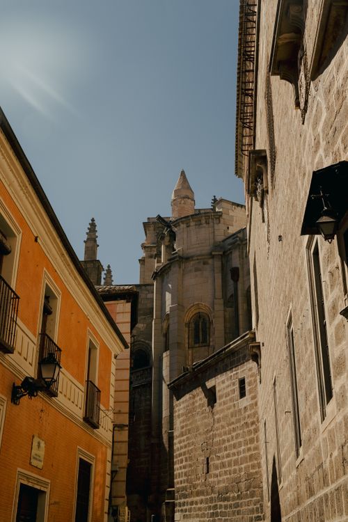 Free A narrow street view highlighting historic European buildings and a cathedral under a bright blue sky. Stock Photo