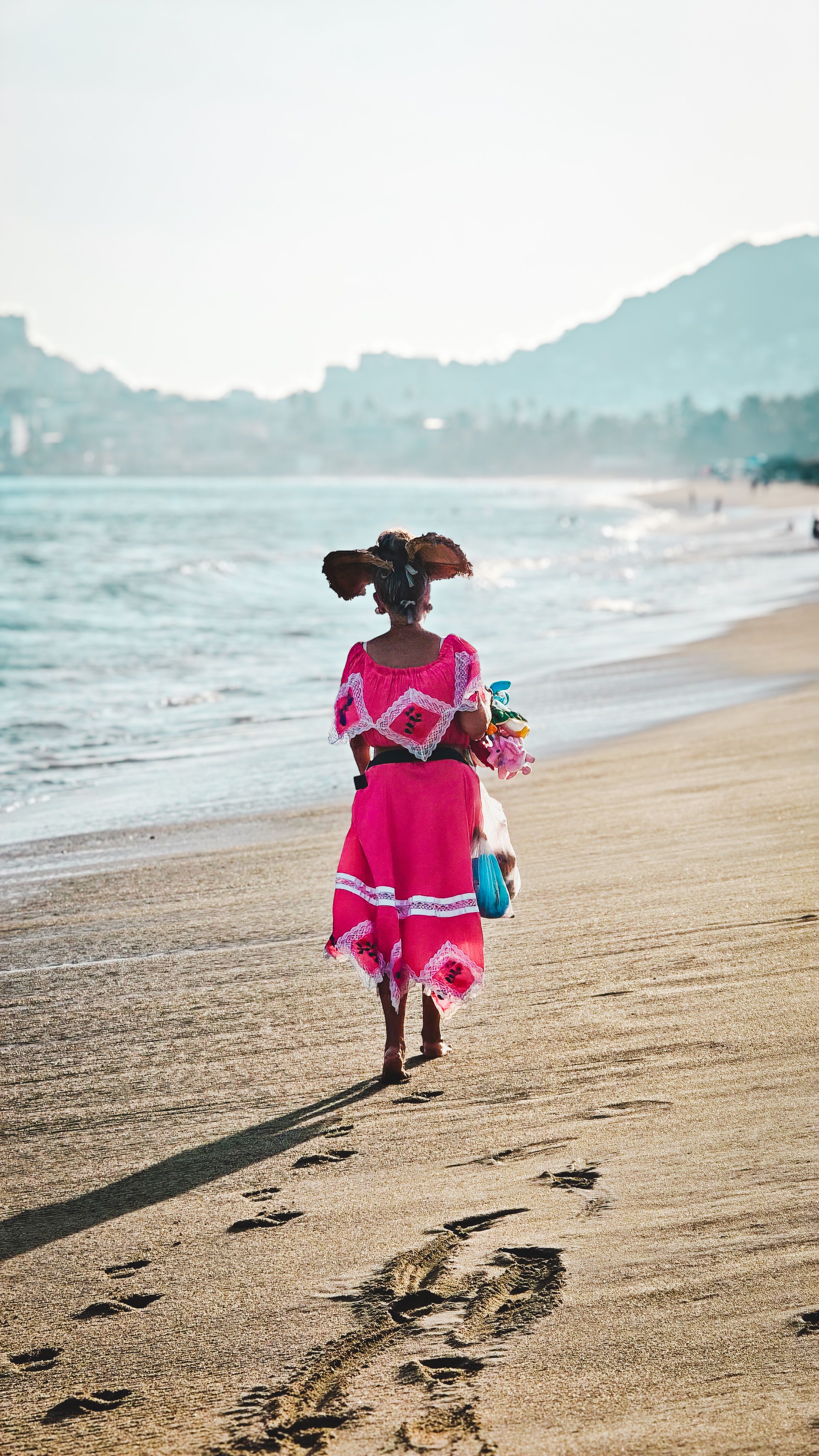 Woman in traditional attire walks along a scenic Mexican beach at sunset, embracing cultural heritage.