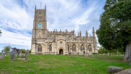 Free Stunning Gothic church with clock tower surrounded by a serene rural landscape. Stock Photo