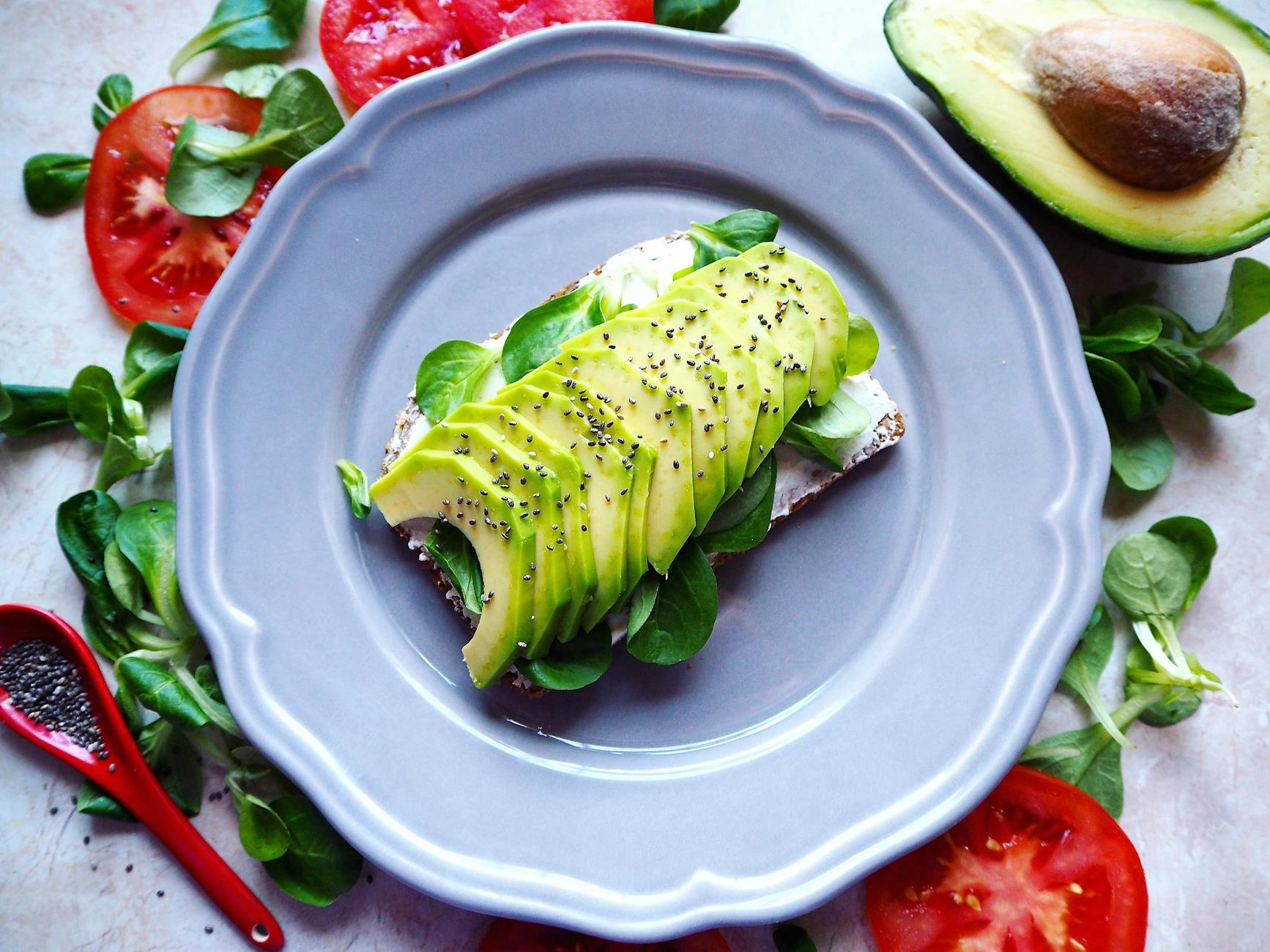 Delicious avocado toast with chia seeds and fresh tomatoes on a grey plate.