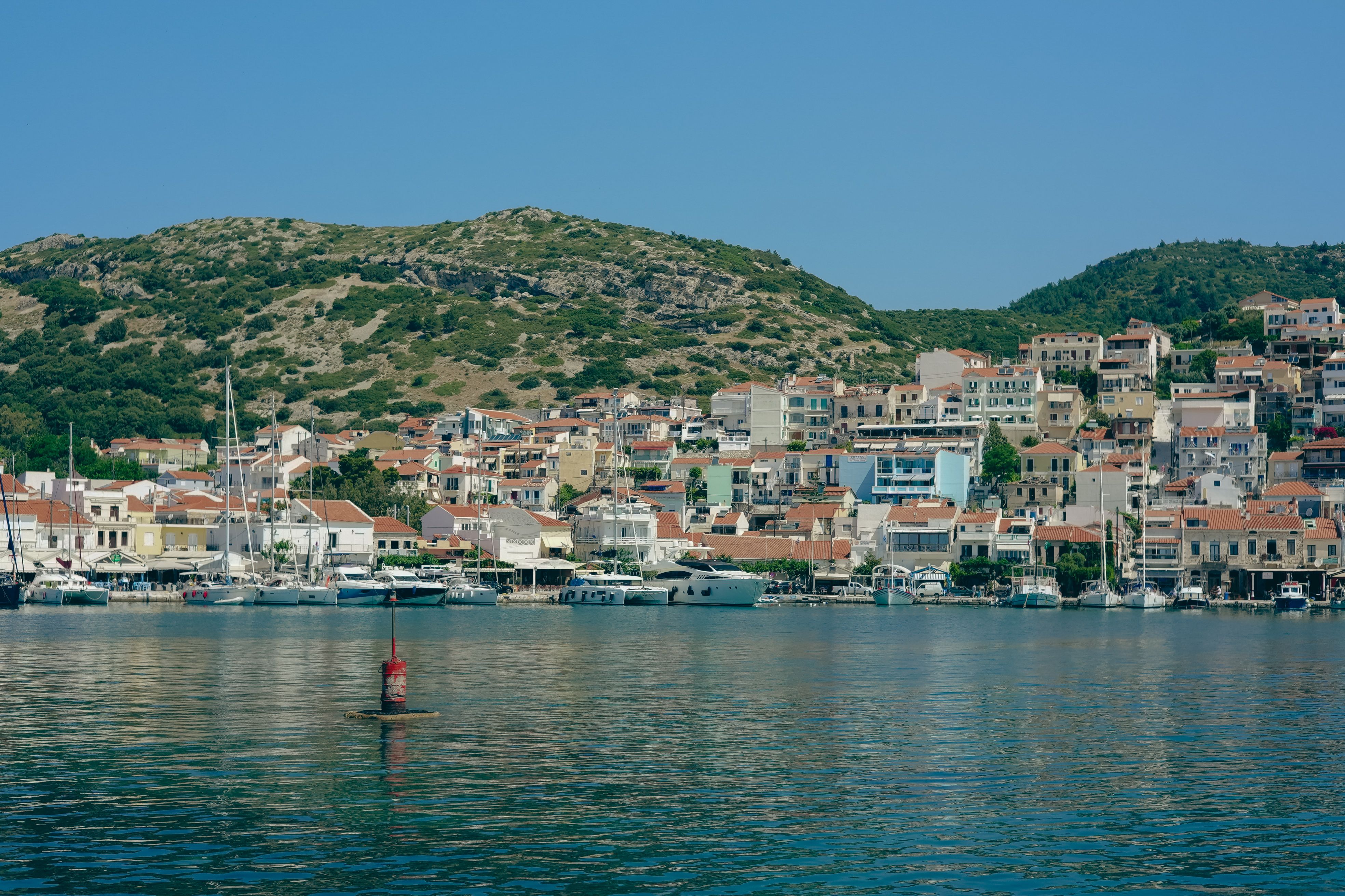 Picturesque coastal town with hillside background and boats docked in harbor under a clear blue sky.