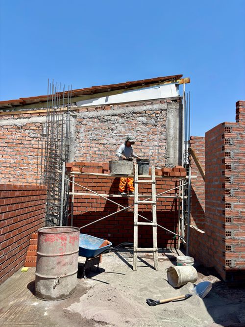 Free Builder working on a brick wall at a construction site, showcasing tools and materials under a clear blue sky. Stock Photo