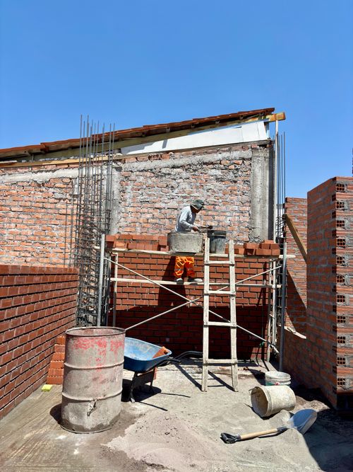 Free Builder laying bricks on scaffold at sunny construction site, surrounded by red brick walls. Stock Photo