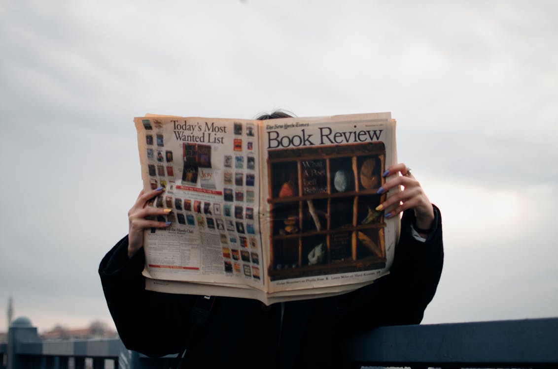 Person Holding White and Brown Newspaper titled "Book Review"