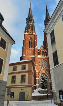 Snow-covered view of Uppsala Cathedral's Gothic spires framed by nearby buildings.
