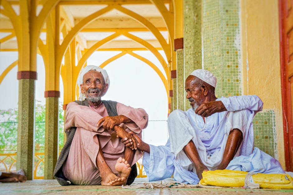 Two elderly men in traditional attire having a conversation in an Eritrean mosque with beautiful architecture.