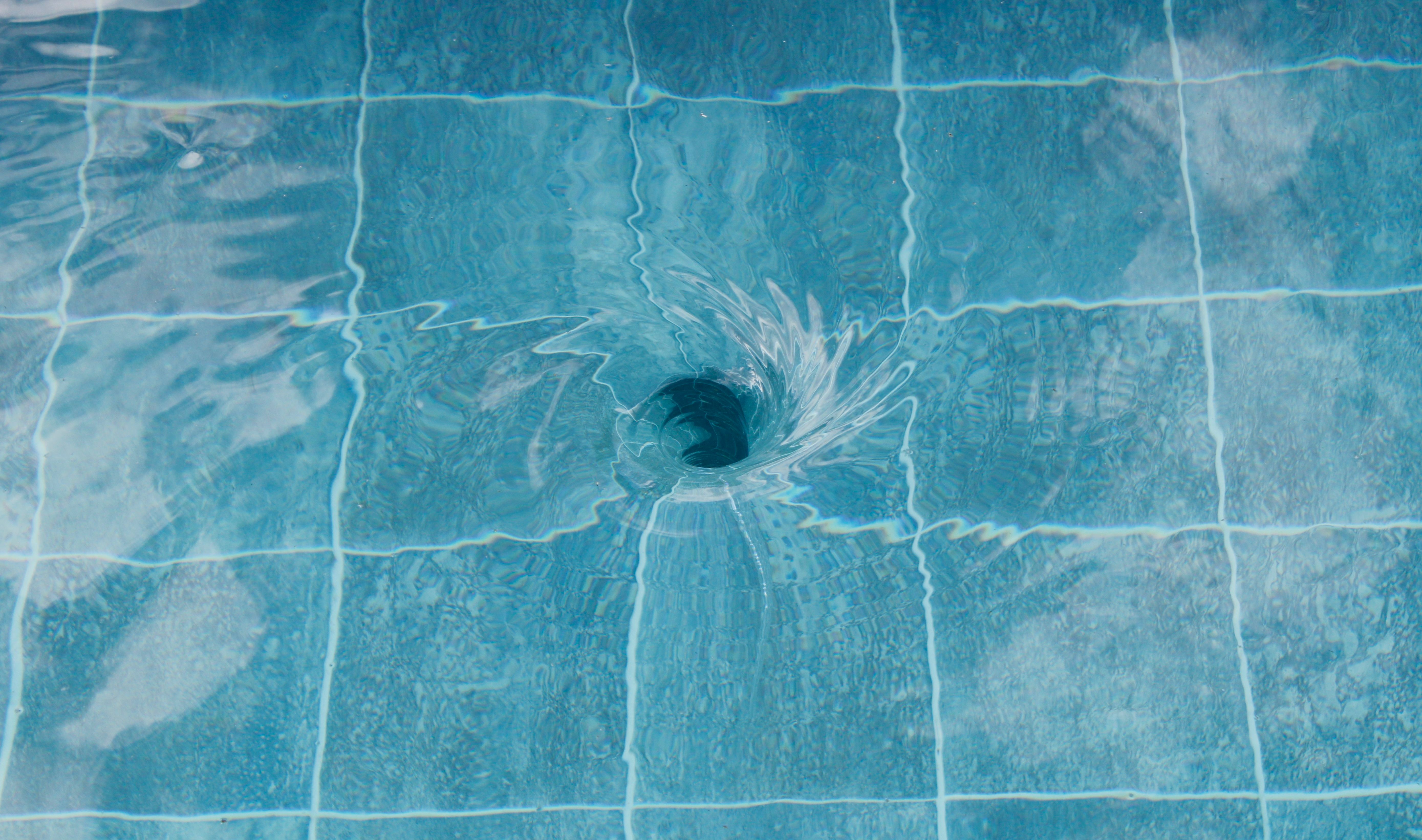 Close-up of water swirling down into a drain over tiles.