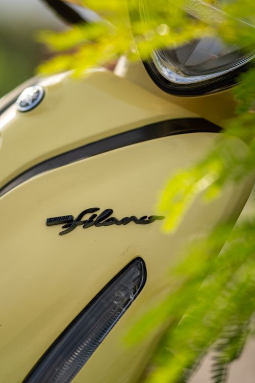 Free Detailed view of a yellow scooter's front headlight and emblem with greenery in the foreground. Stock Photo