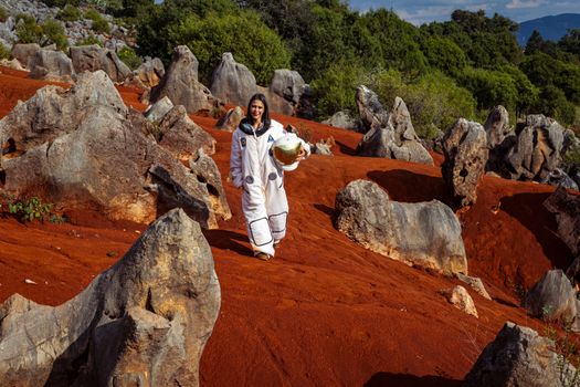 Astronaut in space suit exploring rocky, earth-like terrain with red soil and greenery.