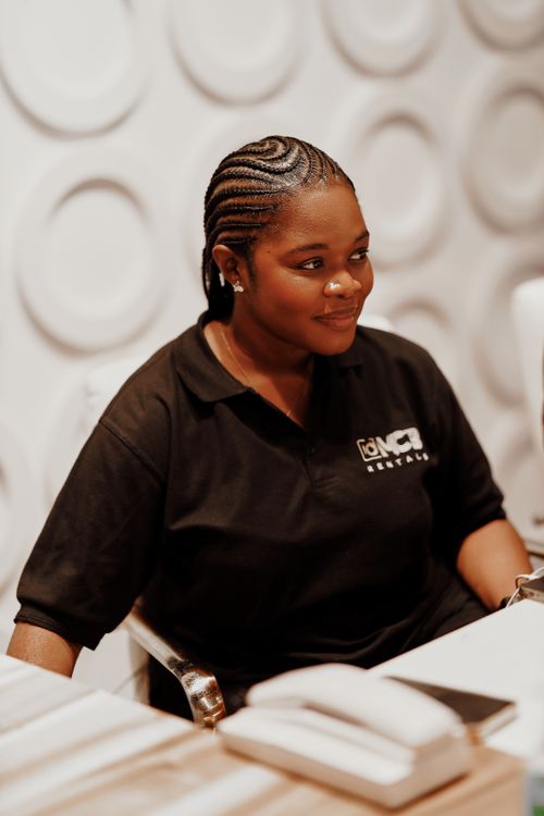 Free A woman in a uniform smiles while seated at a desk indoors with a textured wall background. Stock Photo