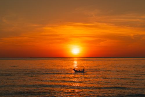 Free A tranquil sunset casts vibrant hues over a peaceful ocean with a silhouetted boat. Stock Photo