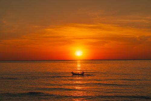 Free A calming sunset scene featuring a small boat on the sea in Quảng Trị, Vietnam, with vibrant orange skies. Stock Photo
