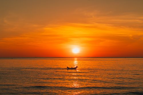 Free A serene sunset view with a boat on the ocean in Quảng Trị, Vietnam, displaying vivid orange hues. Stock Photo