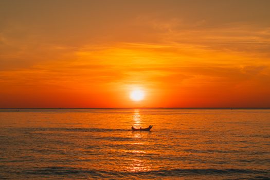 Solitary small boat glides on golden rippling sea at orange sunset