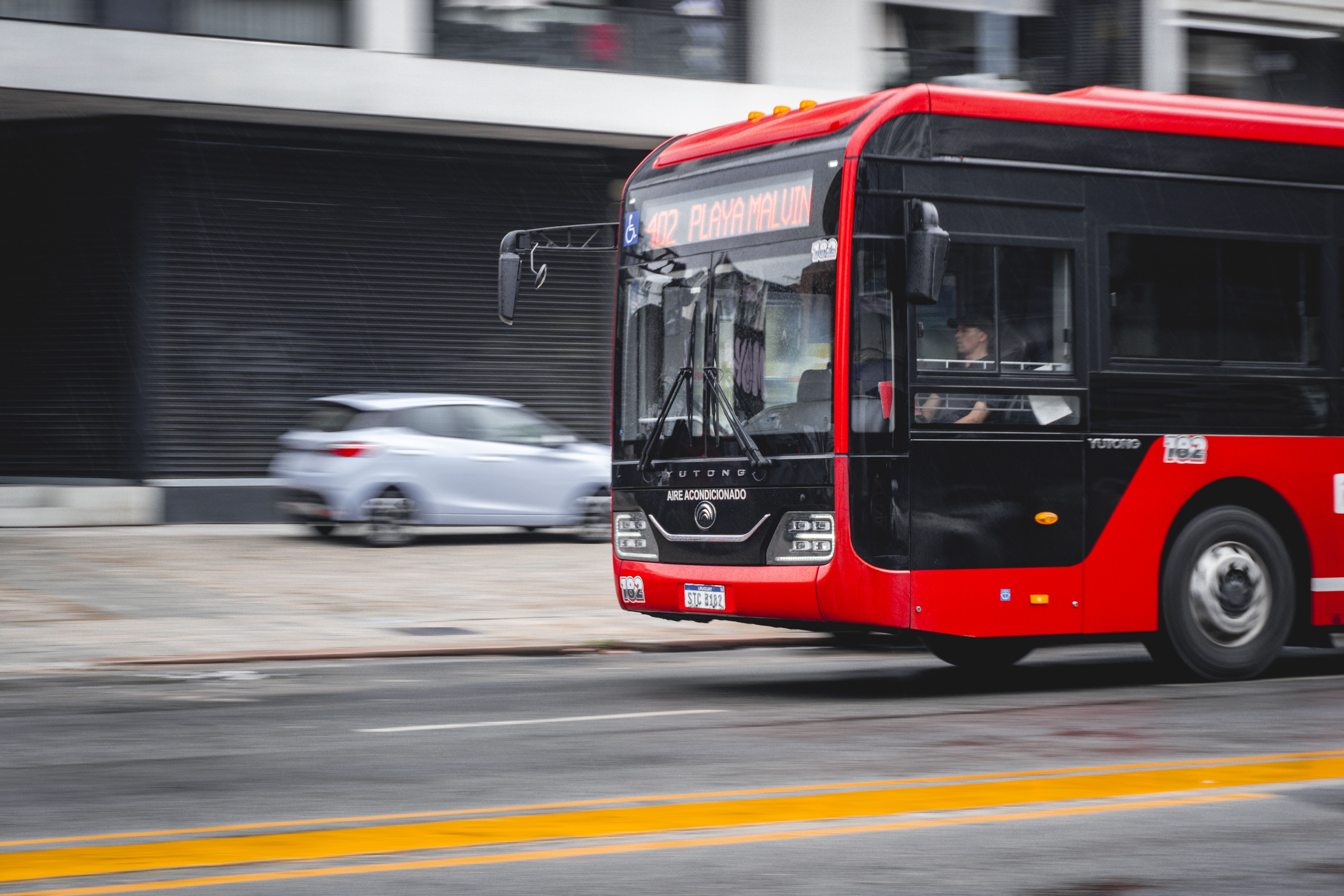 A Red Public Bus Speeding On An Urban Street In Montevideo, Uruguay, Showcasing City Transportation.