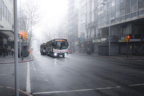 Free City buses navigate through a foggy street in Montevideo, creating an atmospheric urban scene. Stock Photo