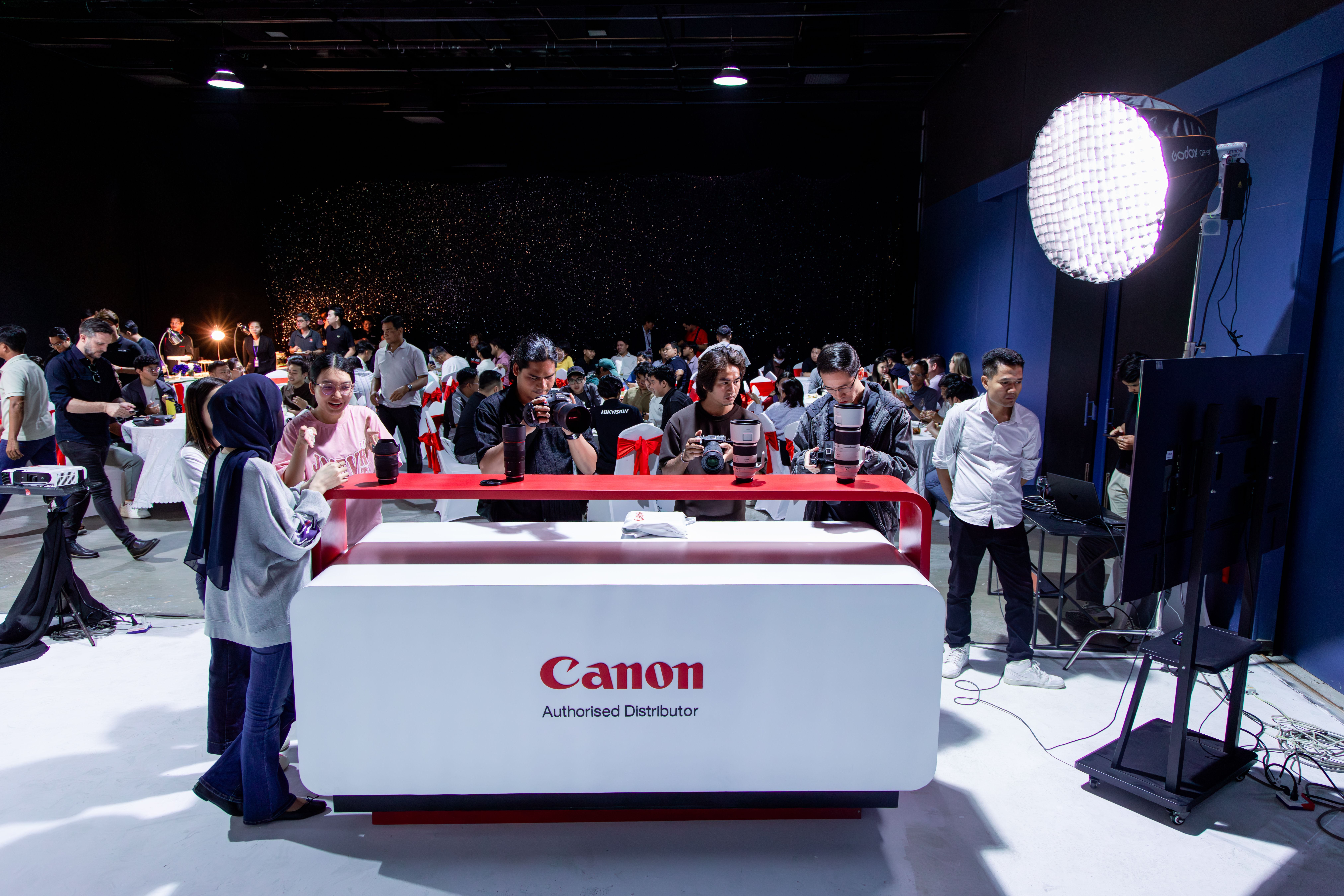 Photographers gather at a Canon photography workshop indoors, engaging with equipment.
