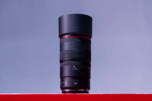 Free Black camera lens standing upright on a vibrant red surface against a gray background. Stock Photo