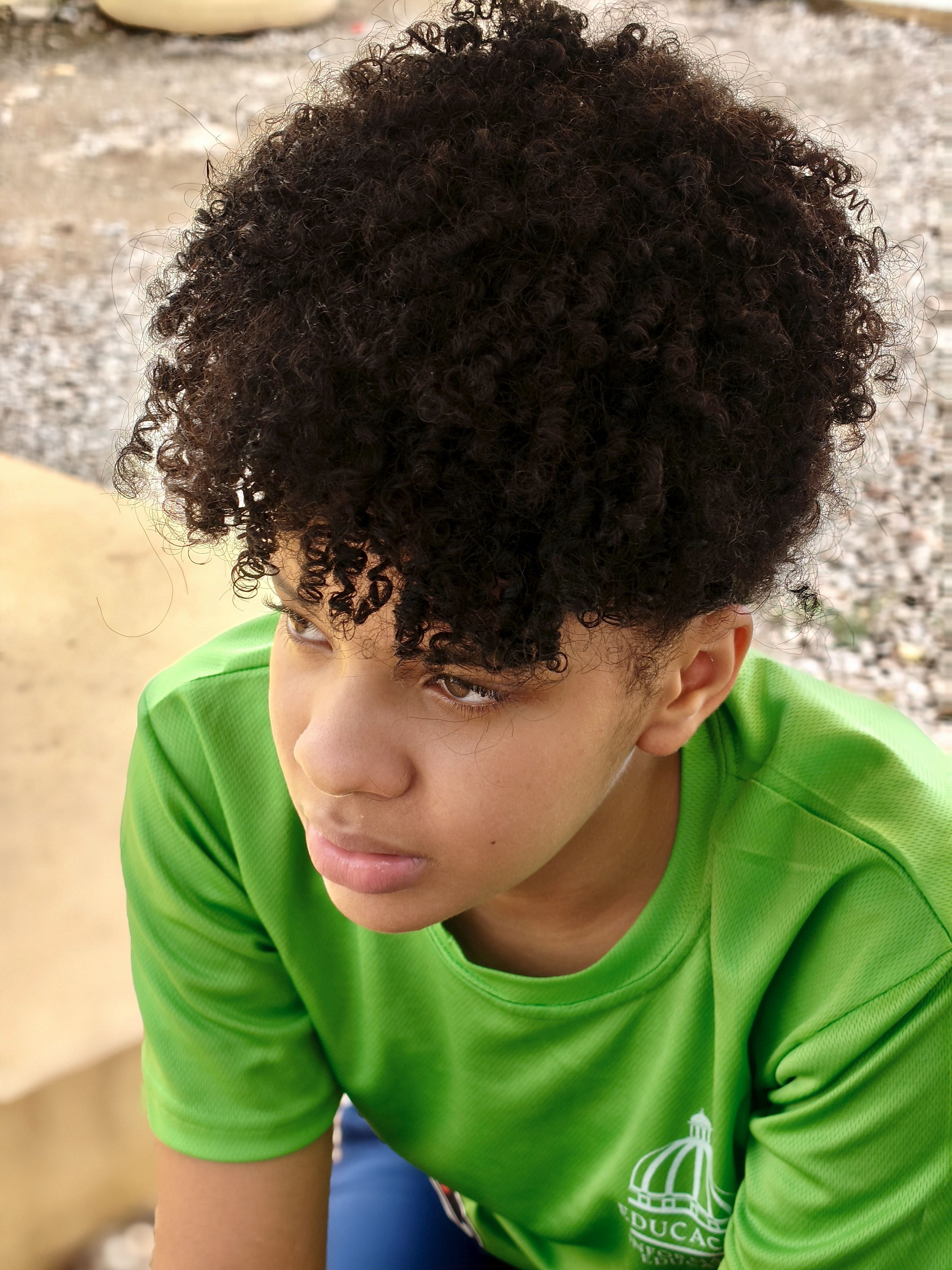 Portrait of a teenage boy with curly hair wearing a green shirt, captured outdoors.