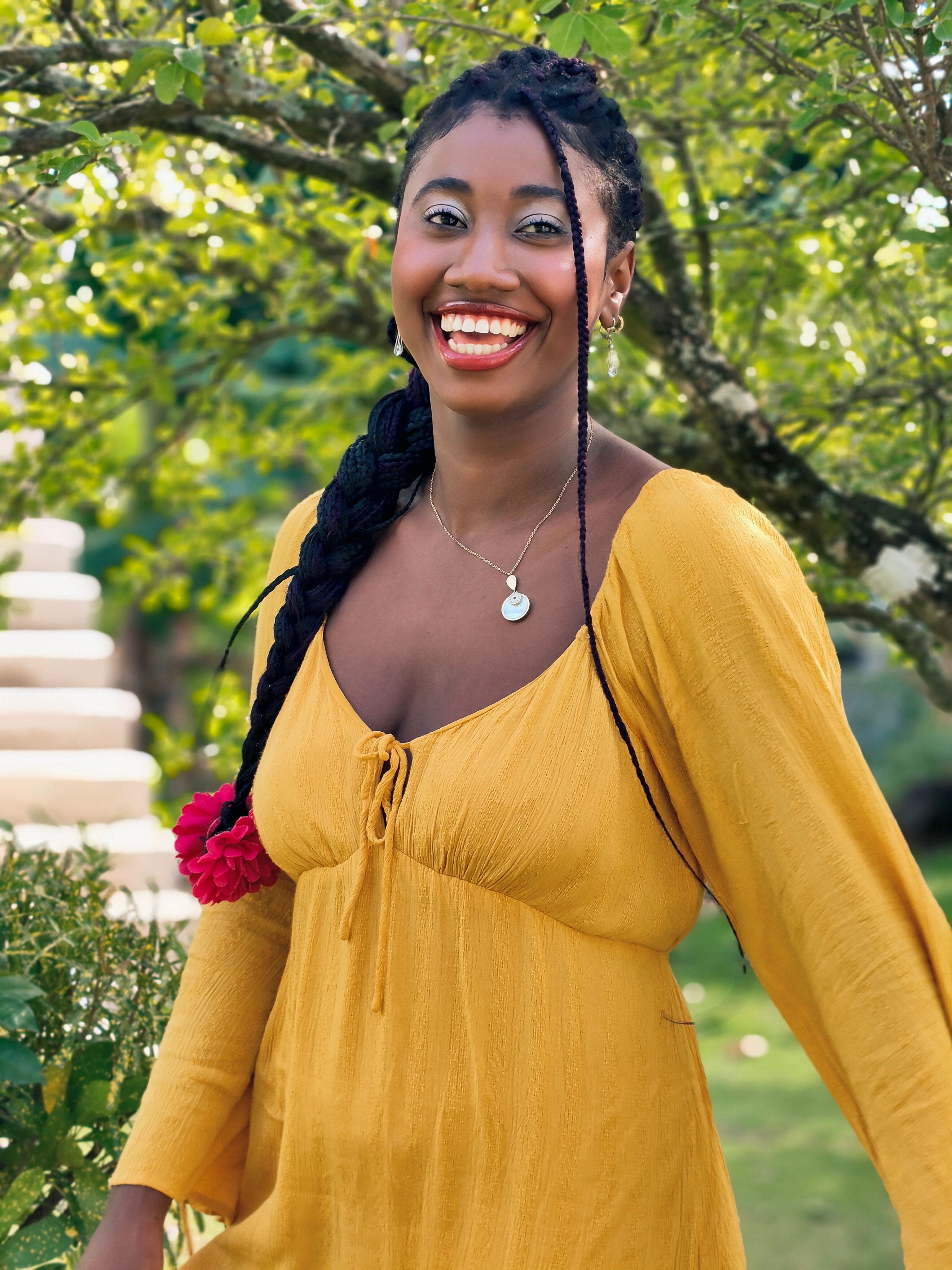 A joyful woman in a yellow dress smiles brightly in a lush garden setting.
