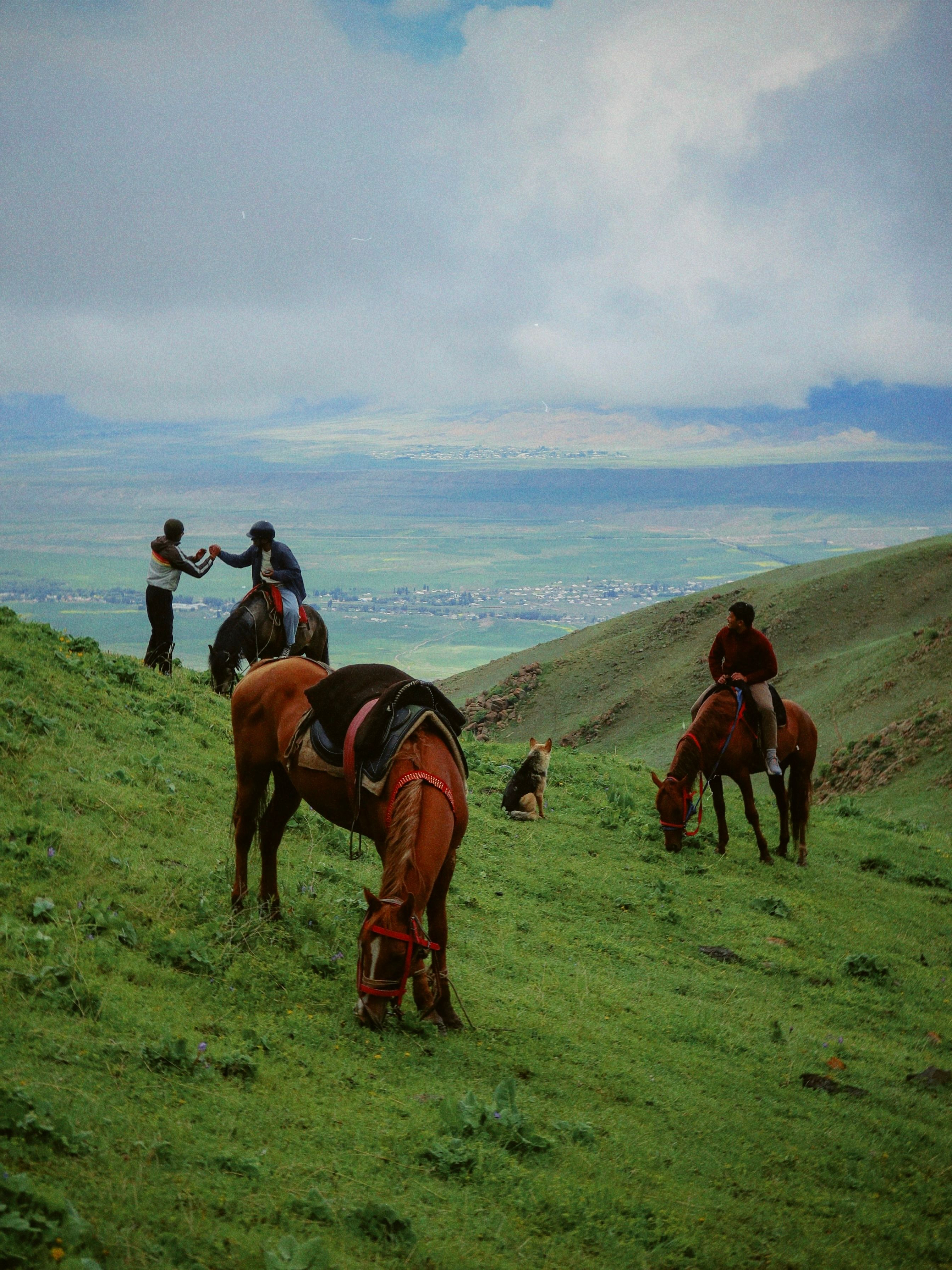 Scenic view of horse riders in the lush green hills of Kyzart, Kyrgyzstan.