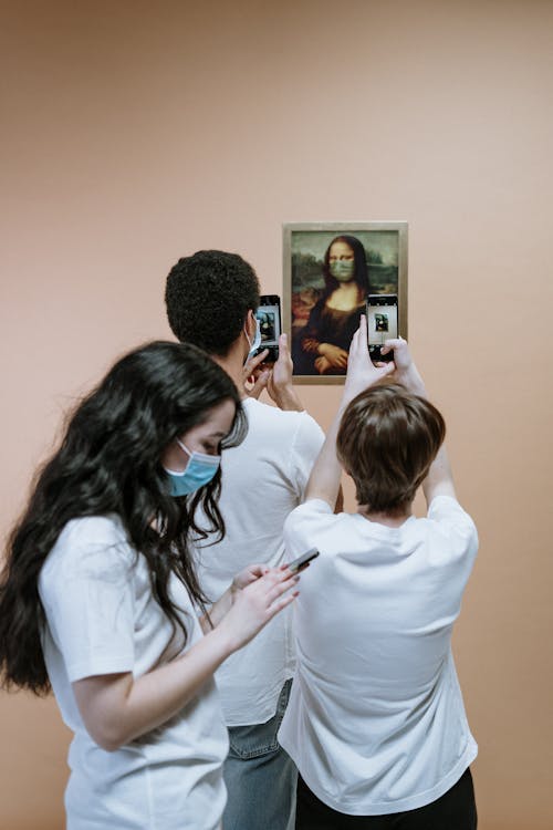 Three People Holding Their Phones And Taking Picture Of A Mona Lisa Painting
