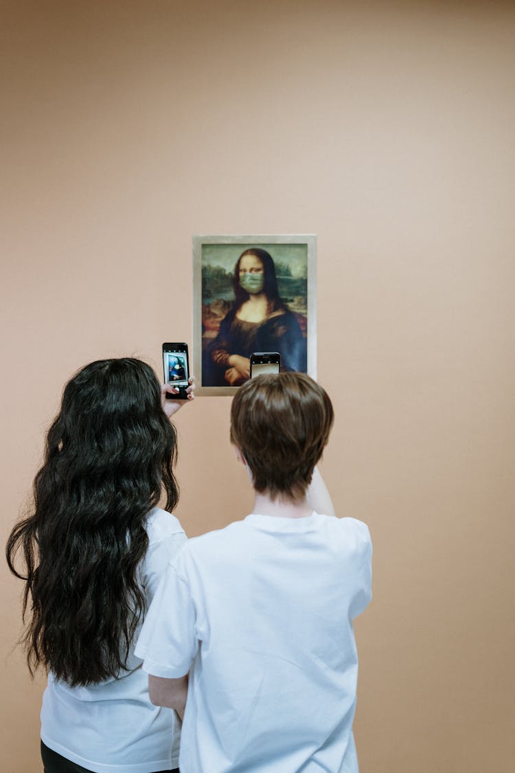 Two Women In White Shirt Taking Picture Of A Painting Of Mona LIsa With Face Mask