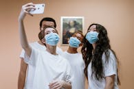 一群年轻人在室内戴着口罩自拍，背景是蒙娜丽莎的画作