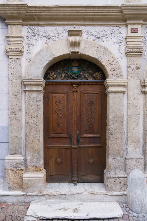 Free A beautifully carved wooden door set in an ornate stone archway, capturing Swiss architectural elegance. Stock Photo