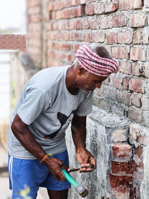 Free Elderly man repairing a brick wall with hammer and chisel, showcasing craftsmanship. Stock Photo