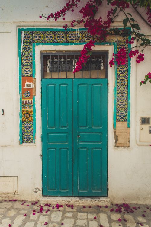Free A vivid turquoise doorway in Tunisia adorned with colorful tiles and bougainvillea. Stock Photo