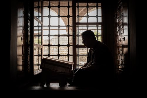 Free Silhouette of a man reading in front of a decorative window, capturing an introspective moment. Stock Photo