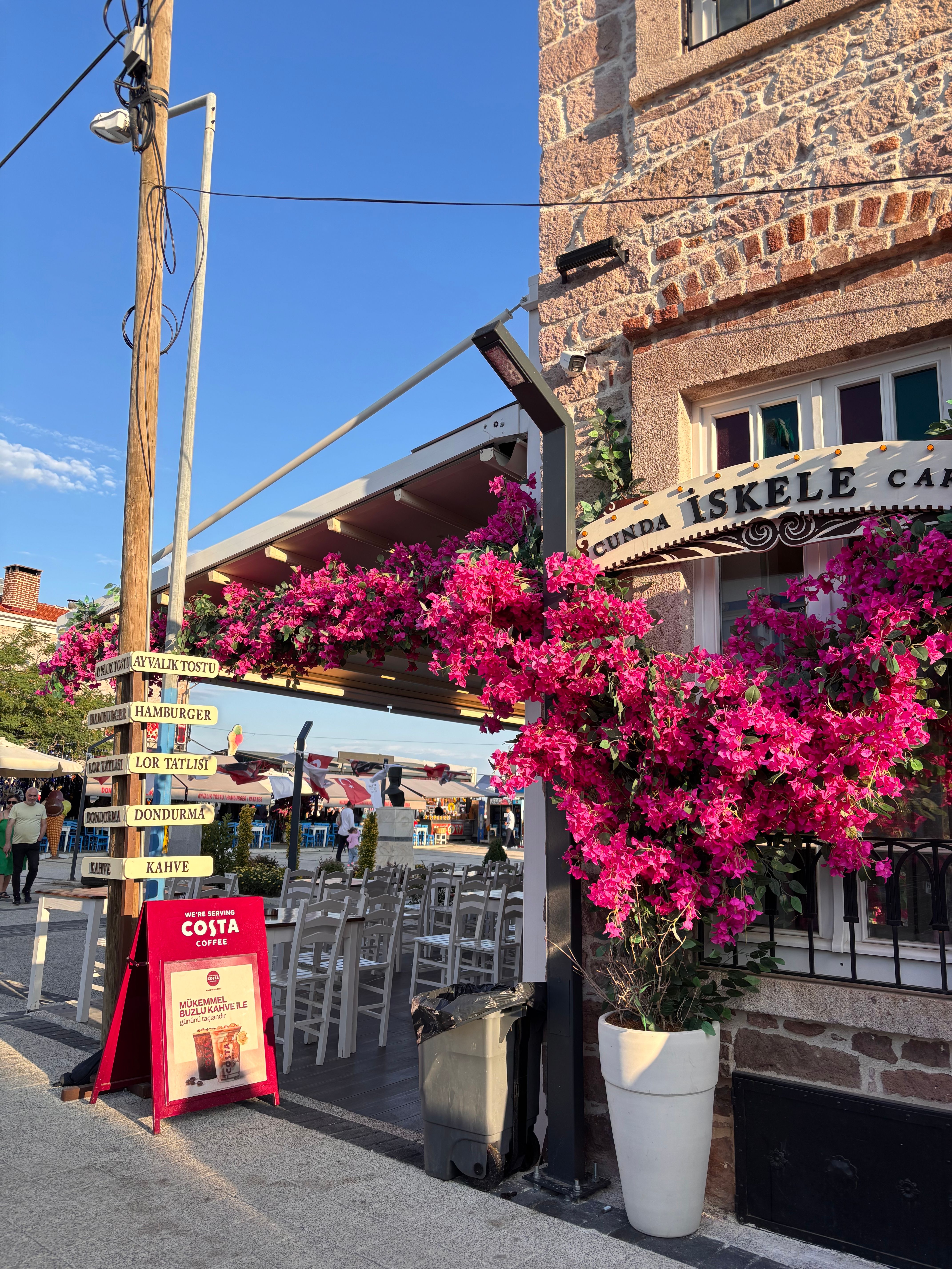 A picturesque café in Ayvalık, Turkey adorned with vibrant pink bougainvillea flowers on a sunny day.