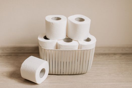 Basket of white toilet paper rolls neatly arranged on a wooden floor.