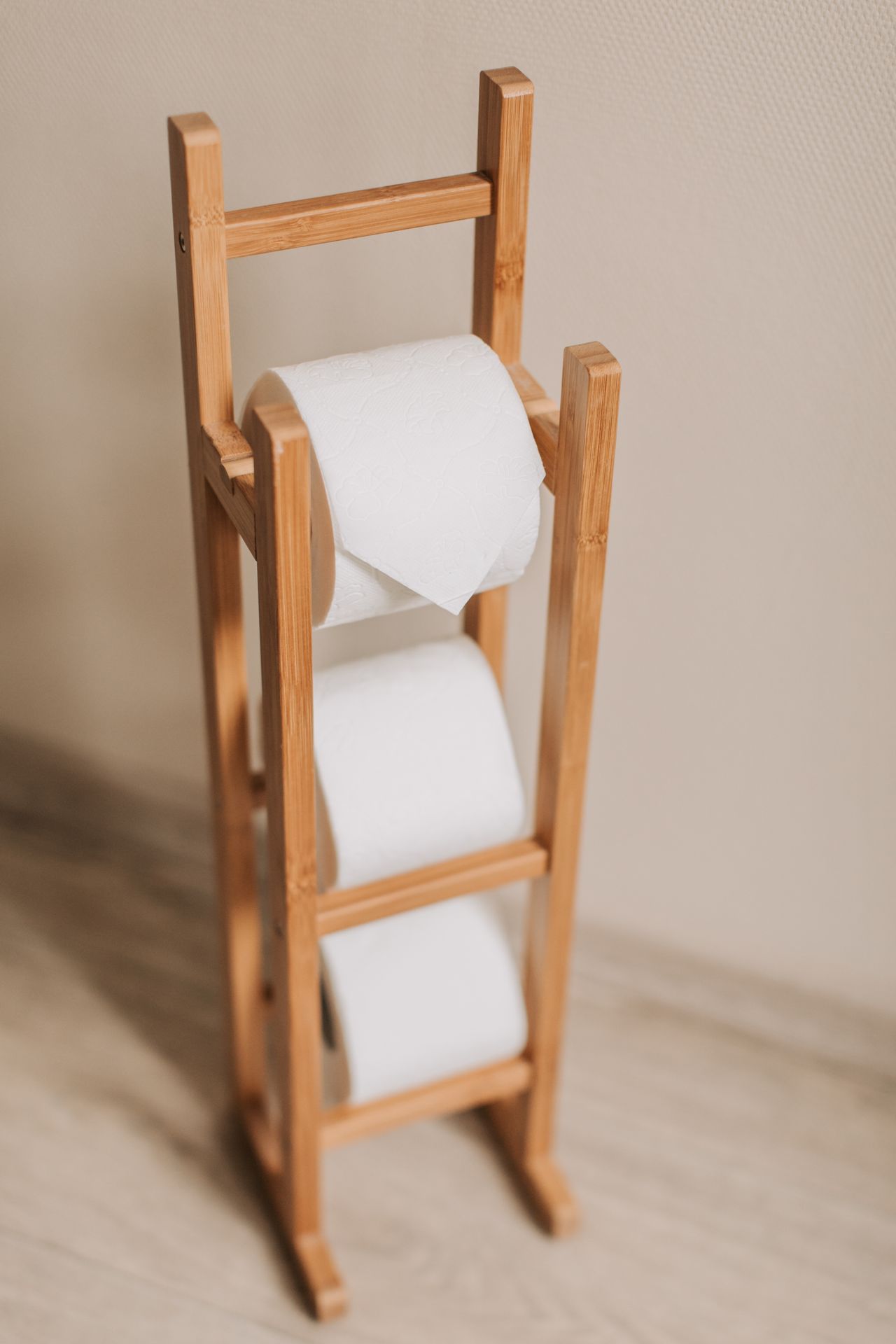 Wooden standing rack holding three rolls of toilet paper