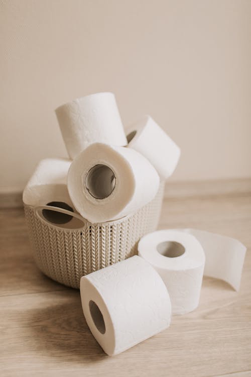 Free White toilet paper rolls placed inside plastic basket and near it on light wooden floor near wall as everyday need for hygiene and sanitary purposes Stock Photo