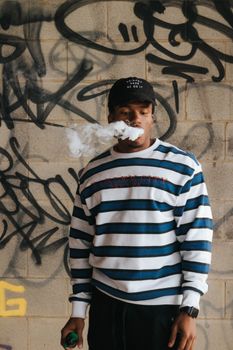 Young man vaping against a graffiti wall. Street style with smoky effect, perfect for urban lifestyle themes.