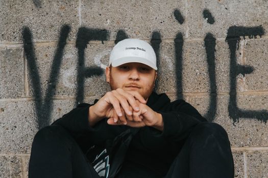 Adult male in front of graffiti wall wearing a cap with political statement. Urban and edgy portrait style.