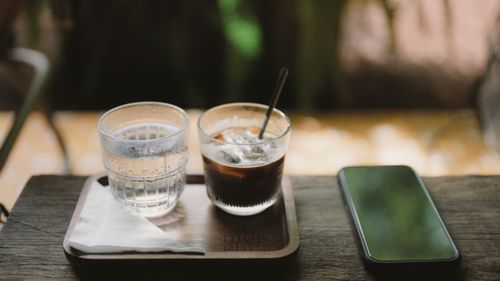 Free A cozy setting with iced coffee, water glass, and smartphone on a wooden tray. Stock Photo