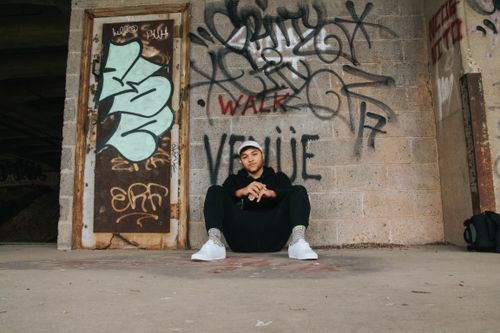 Free A man sits against a wall adorned with vibrant graffiti, embodying street culture. Stock Photo