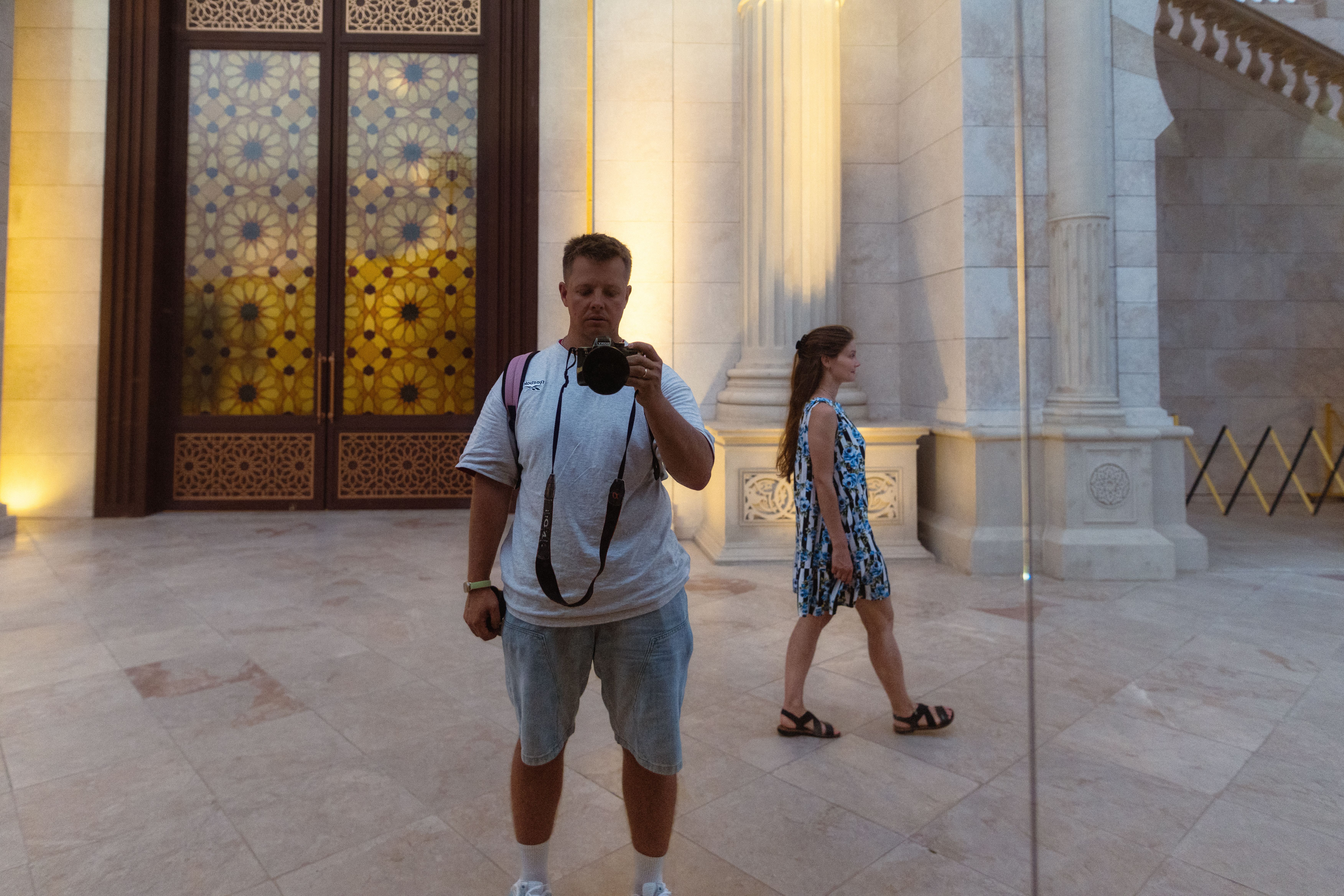 A photographer captures his reflection at Al Noor Mosque, Sharjah, UAE with intricate architectural details.