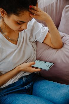 Teenager deeply engaged with smartphone while sitting indoors on comfortable sofa.