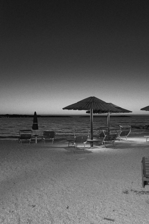 Free Black and white image of a quiet beach at twilight with empty loungers and parasols. Stock Photo