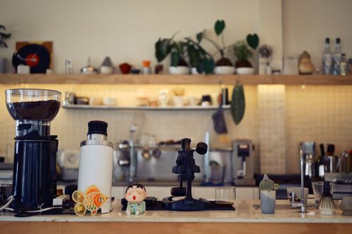 Free A coffee shop counter with coffee grinder, espresso tools, and decorative items creating a warm, inviting atmosphere. Stock Photo